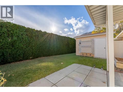 Backyard lawn is bordered by tall hedging, with a shed visible beyond. at 145 REDWING Place Unit# 7, Oliver